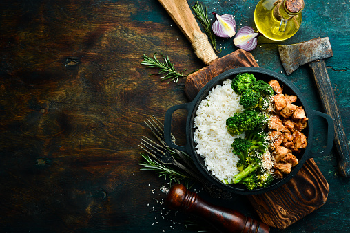 Healthy food. Chicken with teriyaki sauce, boiled rice and broccoli in a black pan. Rustic style. Top view.