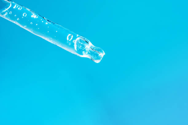 istock Glass dropper with face serum and bubbles on light blue background macro. Transparent pipette with skin care treatment. Aloe vera gel or essential oil for advertising. Hyaluronic acid. Front view 1347194664