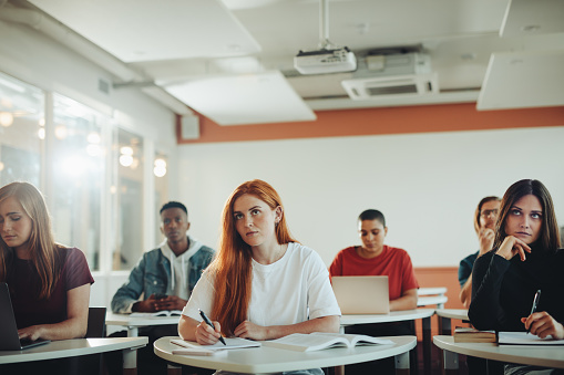 Beautiful teenage student paying attention to lecture in the class. Woman studying in the university classroom.