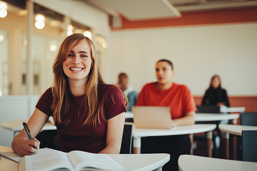 Portrait of beautiful student in high school classroom. Girl in colleague classroom looking at camera and smiling.
