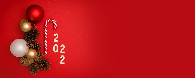 New Year card. Christmas banner mockup with new year balls, pine cones, sandy cane and 2022 numbers on red background with place for text. View from above. Horizontal format.