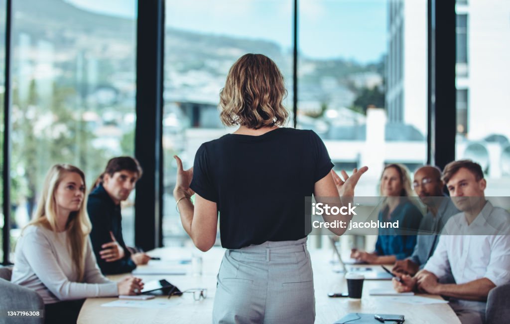 Businesswoman sharing new ideas in meeting Rear view of a woman explaining new strategies to coworkers during conference meeting in office. Businesspeople meeting in office board room for new project discussion. Leadership Stock Photo