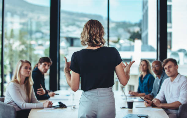 Businesswoman sharing new ideas in meeting Rear view of a woman explaining new strategies to coworkers during conference meeting in office. Businesspeople meeting in office board room for new project discussion. presentation speech stock pictures, royalty-free photos & images