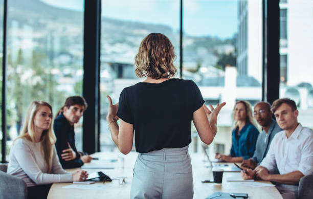 Businesswoman sharing new ideas in meeting Rear view of a woman explaining new strategies to coworkers during conference meeting in office. Businesspeople meeting in office board room for new project discussion. leadership stock pictures, royalty-free photos & images