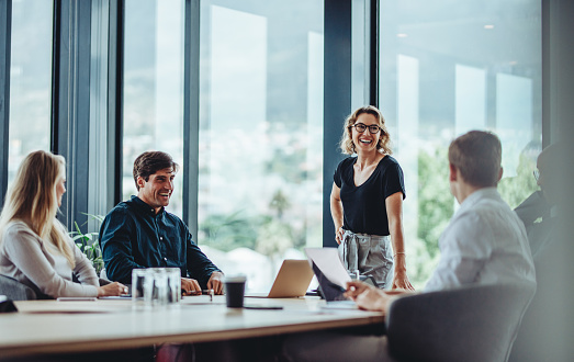 Office colleagues having casual discussion during meeting in conference room. Group of men and women sitting in conference room and smiling.