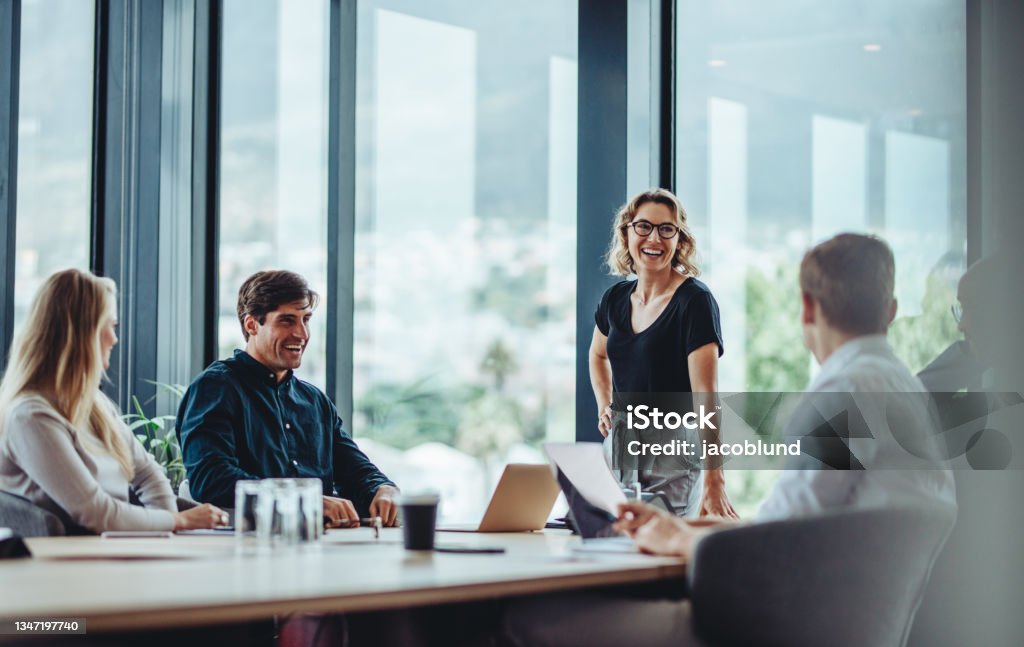 Business people having casual discussion during meeting Office colleagues having casual discussion during meeting in conference room. Group of men and women sitting in conference room and smiling. Office Stock Photo