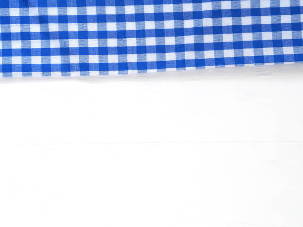 вид сверху, крупным планом из сине-белой клетчатой ткани или салфетки на белом фоне стола. - checked blue tablecloth plaid стоковые фото и изображения