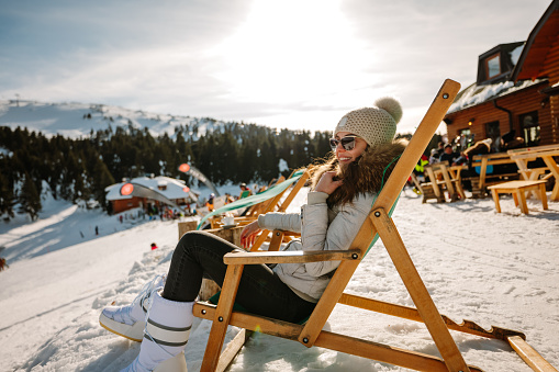 Skier in colorful gear relaxing and sipping a drink at the ski lodge with fellow enthusiasts around.