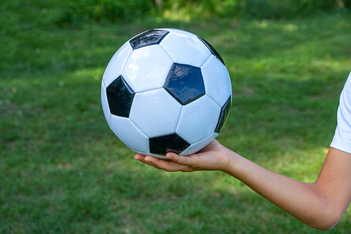 Soccer ball white and black leather in hand of football player on green grass. Background image.