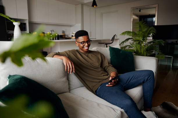istock Young adult black male relaxing on sofa while texting his girlfriend, modern apartment 1347207603
