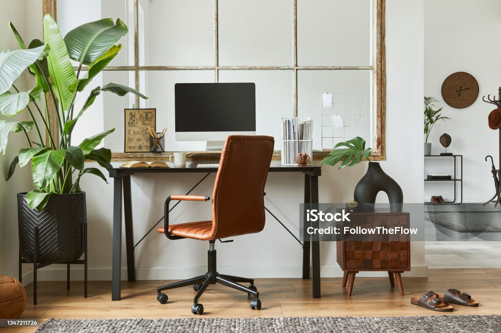 Creative workspace composition of modern masculine home office interior with black industrial desk, brown leather armchair, laptop, vintage record player and stylish personal accessories. Template. Creative composition of modern masculine home office workspace interior with black industrial desk, brown leather armchair, pc and stylish personal accessories. Template. Home Office Stock Photo
