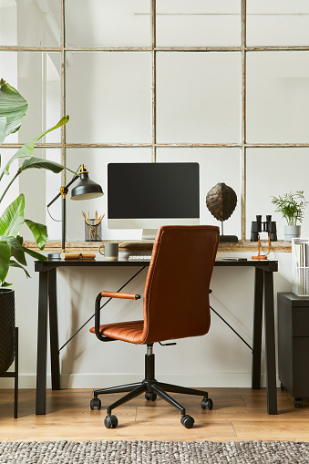 Creative composition of modern masculine home office workspace interior with black industrial desk, brown leather armchair, pc and stylish personal accessories. Template.