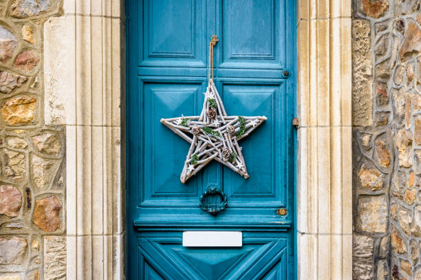 Front view of a star-shape Christmas decoration made of branches and pine cones, hanging on the blue front door with moldings of an old townhouse.