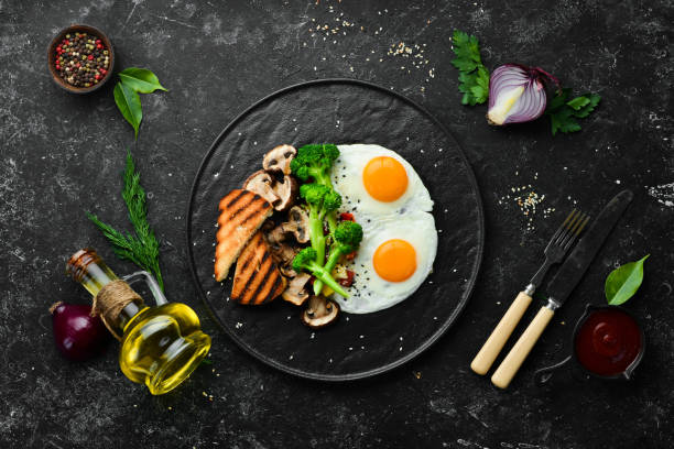 Healthy breakfast. Fried egg with broccoli, mushrooms and bread. On a black stone plate. Top view.