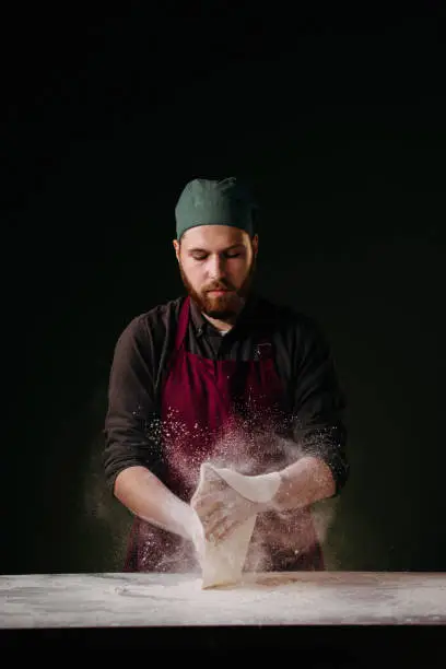 A young caucasian bearded chef spreading some pizza dough