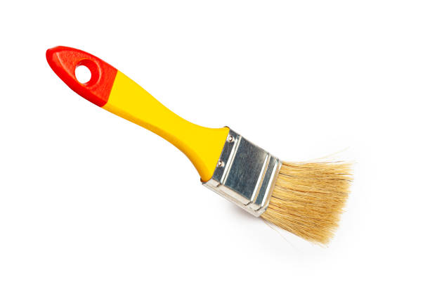 New paint brush levitating over Red Wooden Table. Beautiful yellow wall background behind.