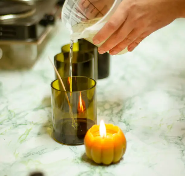 Photo of candle making process, small business concept at home, craftsman pours wax into a mold with a wick.