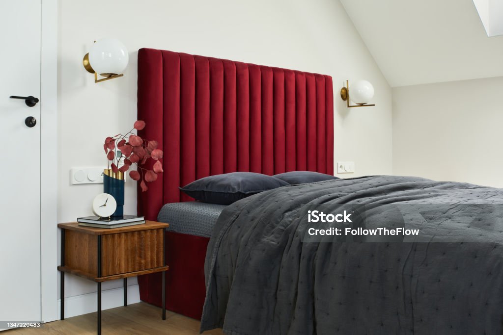 Minimalistic elegant bedroom interior with red bed, grey bedclothes and wooden furniture. Glamour style inspiration. Template. Bedroom Stock Photo