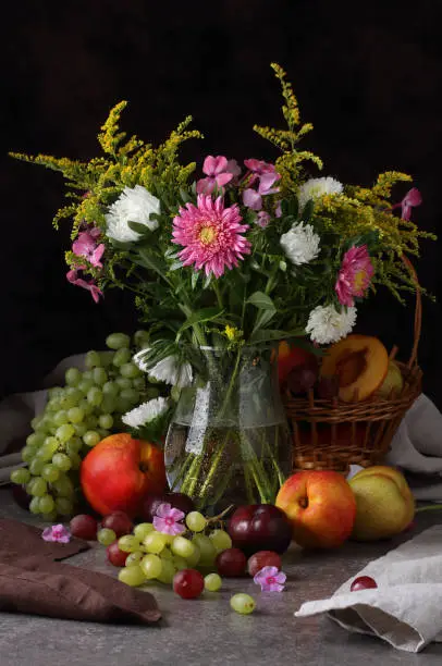 Photo of Still life with a bouquet of flowers and fruits on a dark background