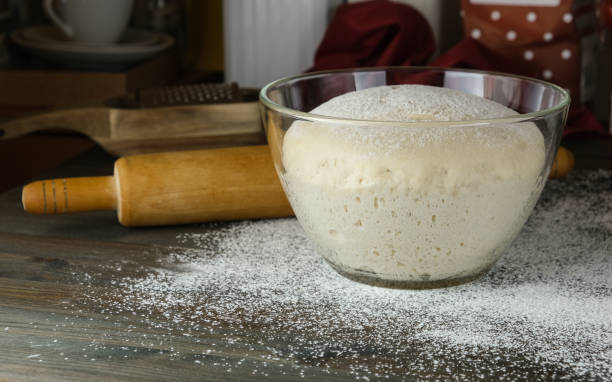sourdough for baking, yeast dough, fermentation, opara in a glass vessel on a table powdered with white flour. Wooden rolling pin and kitchen utensils in the background. process of cooking homemade bread, pizza, pies. masa madre para hornear, masa de levadura, fermentación, opara en un recipiente de vidrio sobre una mesa en polvo con harina blanca. rodillo de madera y utensilios de cocina al fondo. proceso de cocción de pan casero, pizza, pasteles. masa agria.