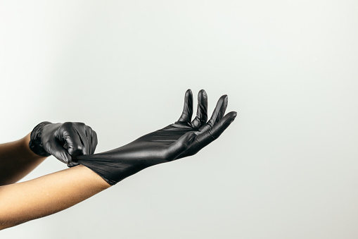 Woman is preparing for her job and putting on black protective gloves. Photo taken with bright background. She is professional permanent make up artist