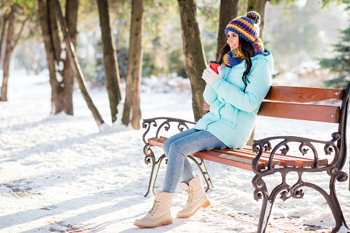 Photo of cute lady hold takeaway cup sit bench drink coffee wear hat scarf gloves coat in winter park outside