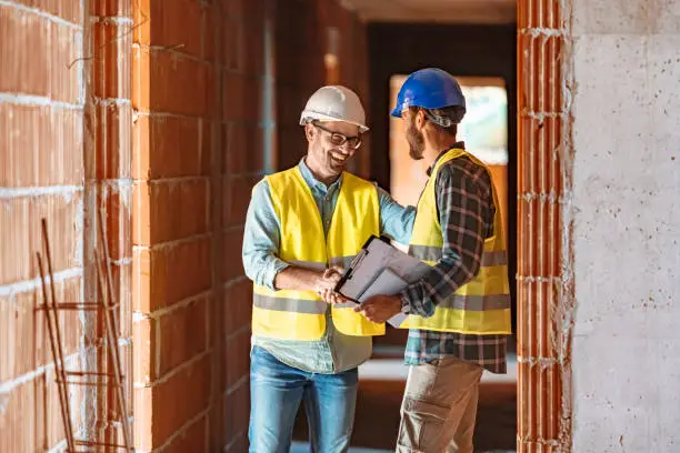 Worker and architect shaking hands at construction site