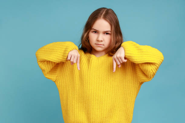 istock Portrait of little girl pointing down, gesturing below with strict angry expression. here and now. 1347227793