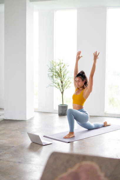 azjatycka kobieta ćwiczące jogę podczas korzystania z laptopa zdjęcie stockowe - stretching yoga exercise mat women zdjęcia i obrazy z banku zdjęć