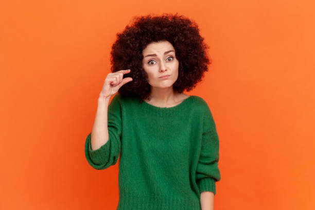 porträt einer frau mit afro-frisur, die einen grünen casual-style-pullover trägt, der eine kleine geste mit den fingern zeigt und enttäuscht in die kamera schaut. - less fortunate stock-fotos und bilder