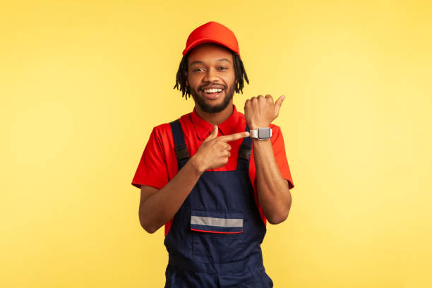 istock Smiling happy courier or mechanic standing pointing at wristwatch, showing work time. 1347228785