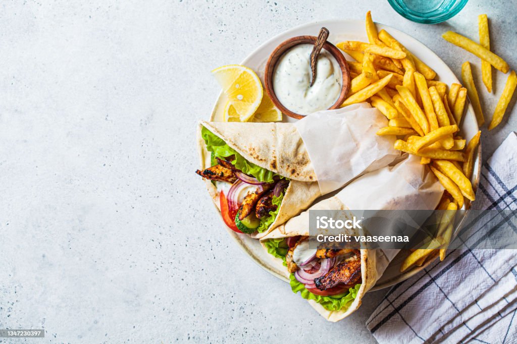 Chicken gyros with vegetables, french fries and tzatziki sauce on plate. Greek food concept. Chicken gyros with vegetables, french fries and tzatziki sauce on a plate, top view. Greek food concept. Shawarma Stock Photo