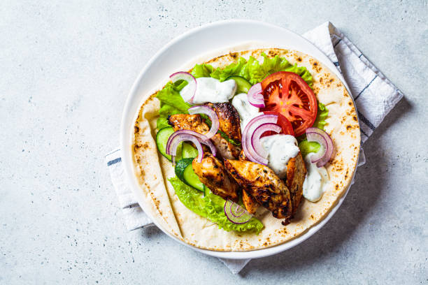 Cooking chicken gyros with vegetables and tzatziki sauce. Greek food concept. stock photo