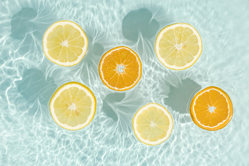 Natural citrus fruit background with fresh, juicy slices of lemon and orange floating in the water. Organic, healthy food and beverages diet concept. Pastel colors pattern. Minimal flat lay.