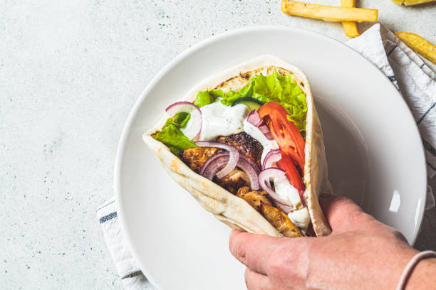 hähnchengyros mit gemüse, pommes frites und tzatziki-sauce in der hand. griechisches essenskonzept. - sandwich plate food french fries stock-fotos und bilder