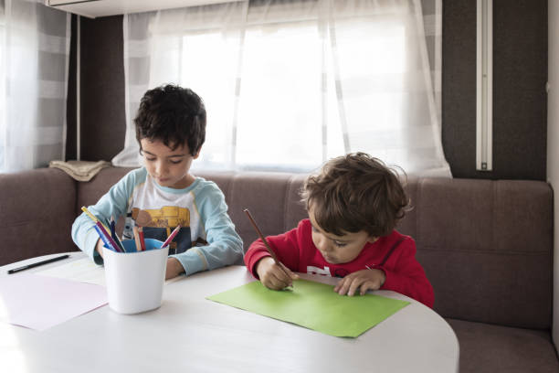 two Caucasian boy paints inside caravan on weekend trip.