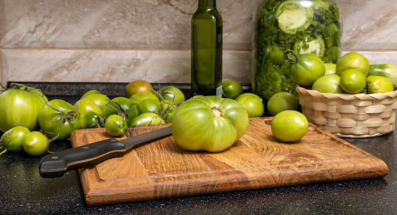 Closeup of green tomatoes on the wooden cutting board and in basket.Process of preparation of green tomatoes preservation
