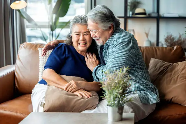 Photo of old senior asian retired couple enjoy talking conversation together on sofa with happiness laugh smile and joyful at home,asian old mature adult stay home quarantine period concept
