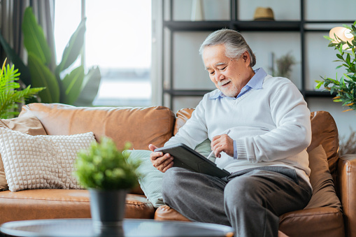 old asian senior grandfather enjoy sunday weekend reading notebook on sofa couch at home,home isolation senior male adult relax casual happiness at home