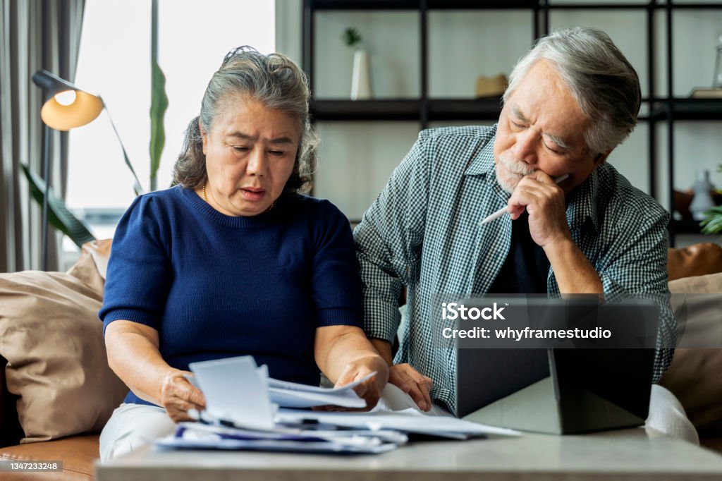 Serious stressed asian senior old couple worried about bills discuss unpaid bank debt paper, sad poor retired family looking at tablet counting loan payment worry about money problem Retirement Stock Photo