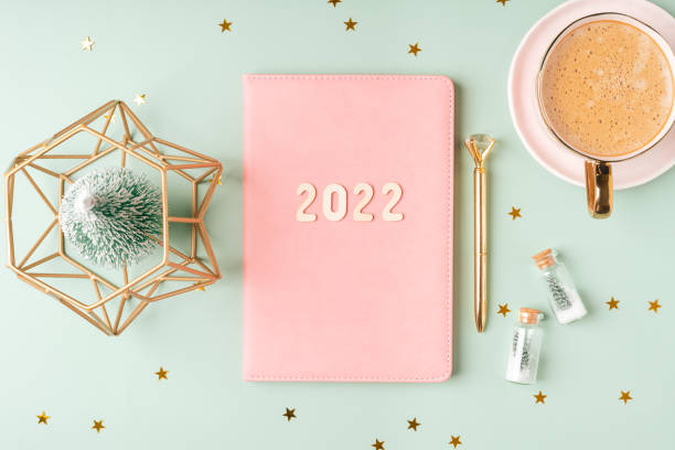 istock Top view Desktop Christmas pink notepad with 2022 letters text. Flat lay on green mint table background with planner, cup of coffee, candle, Christmas decoration, notebook and stationery 1347233583