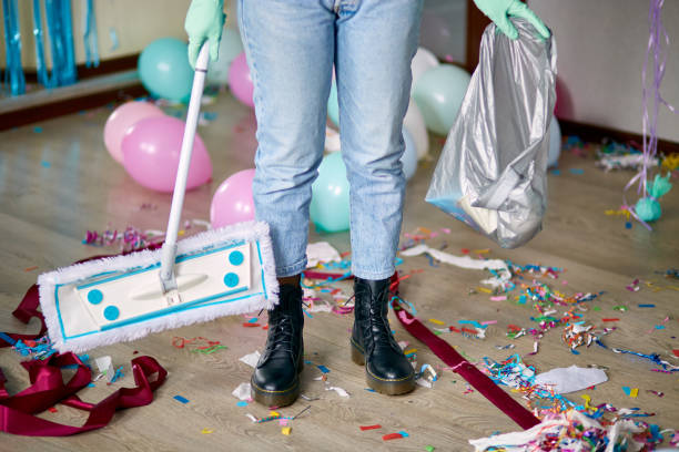 Woman with pushbroom cleaning mess of floor in room after party confetti Woman with pushbroom cleaning mess of floor in room after party confetti, morning after party celebration, housework, cleaning service after party stock pictures, royalty-free photos & images