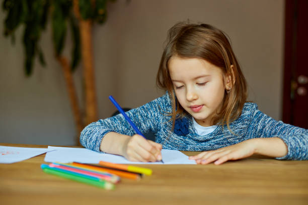 istock School girl drawing and writing a picture with crayons, using colored pencils 1347235174