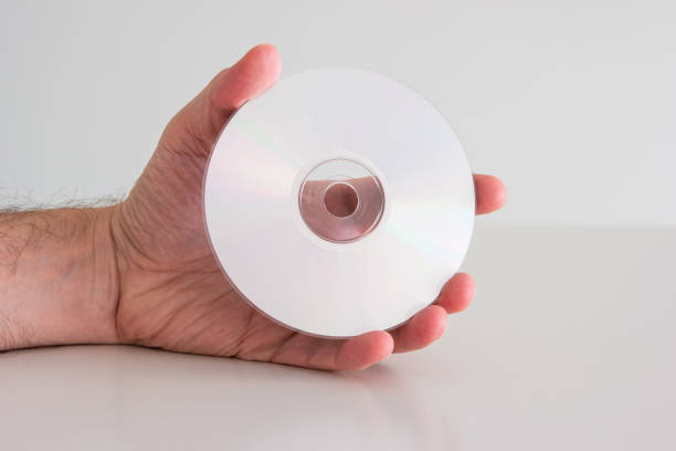 istock Compact Disc DVD held in hand by Caucasian male hand. Writable side view, close up studio shot, isolated on white 1347239705