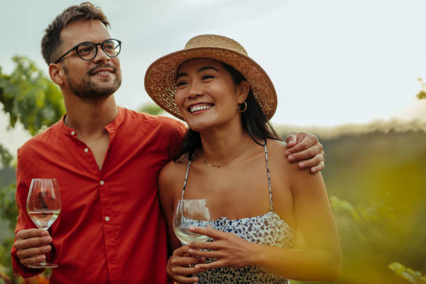 As good as nature intended Diverse couple enjoying a glass of wine while walking through the vineyard winery stock pictures, royalty-free photos & images