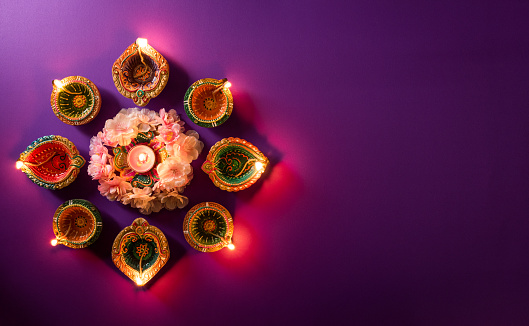 Happy Diwali - Clay Diya lamps lit during Dipavali, Hindu festival of lights celebration. Colorful traditional oil lamp diya on purple background