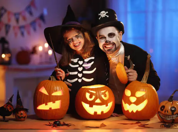 Photo of Happy family father and daughter in Halloween costumes   with glowing jack-o-lantern celebrating all hallows eve at home