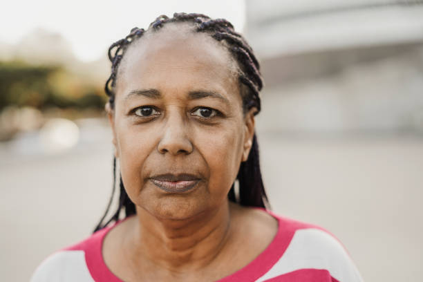 femme africaine âgée regardant la caméra en plein air dans la ville - focus sur le visage - unsmiling photos et images de collection