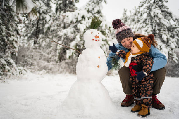 bambino giocoso, che aiuta sua madre a fare un pupazzo di neve - snowman snow winter fun foto e immagini stock