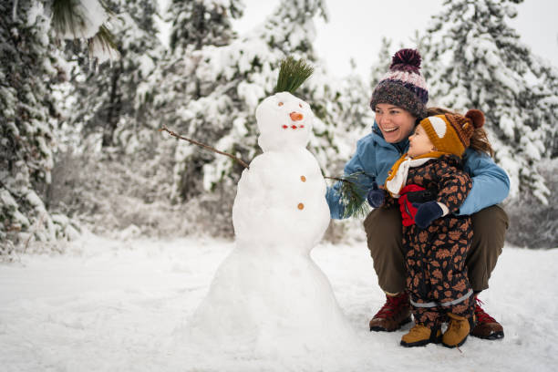 Curious toodler boy observing his mother while she making a snowman stock photo